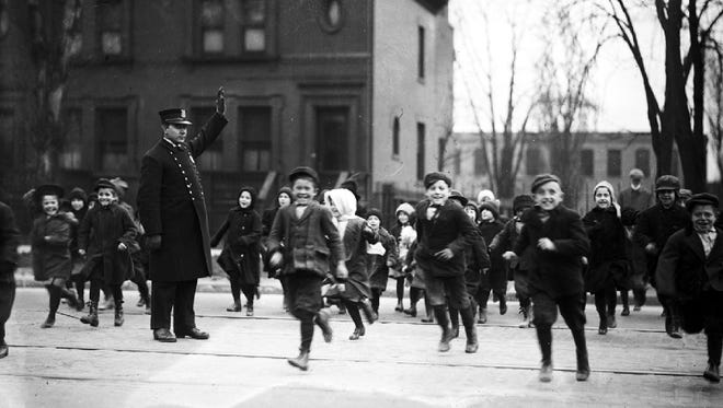 A Detroit police officer stops traffic to let children cross the street when school lets out in 1927.
