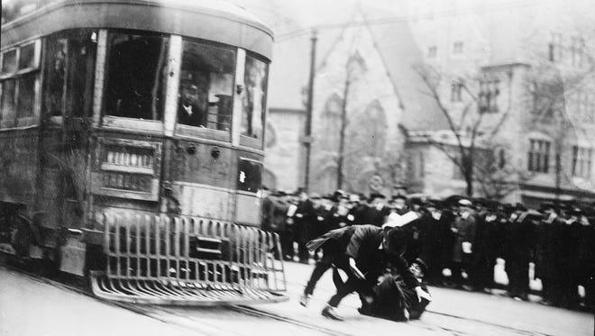 As the demonstration continues, the two men are nudged by the grill on the front of the streetcar and tumble onto the street.