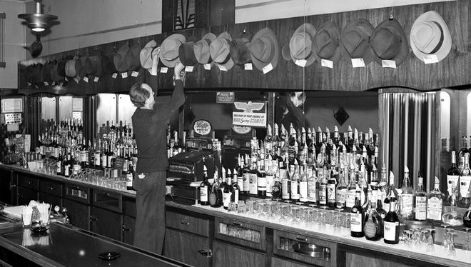 In September 1942, the barkeeper at the Kenwood Bar hangs the hats of customers who have gone into the service during World War II. Signs announce "Blatz on tap" and "Take part of your change in war savings stamps."