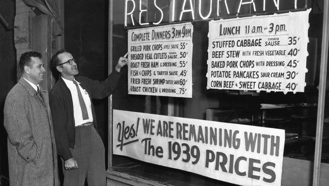 Joseph Tuczak, right, proprietor of a restaurant on Detroit's west side, and his  friend John Bombyk look at the price of meals displayed in the window of Tuczak's eating house on Nov. 23, 1939. The priciest item was roast chicken and dressing, for 75 cents.