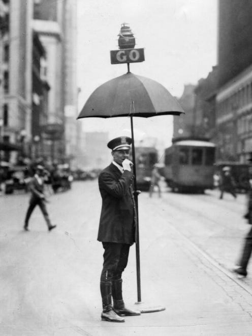 A police officer, shielded somewhat from rain or sun, tweets a whistle for 10 seconds before turning the sign from Go to Stop in 1925. Officers also used hand signals, but many drivers didn't understand them.