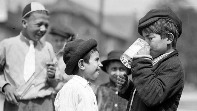 Watched by his pals, a boy drinks a root beer in Detroit in the early 20th century.