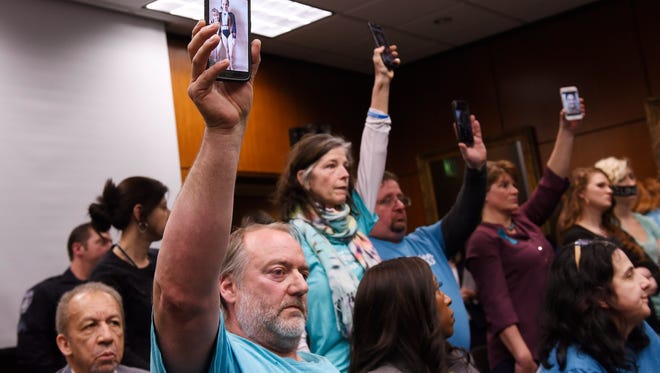 Parents of Nassar-abuse survivors, from left, Glen Black, 53, of Pinckney and Tammy Bourque-Stemas of Dearborn and others hold up pictures of their daughters on their cellphones during the board meeting.