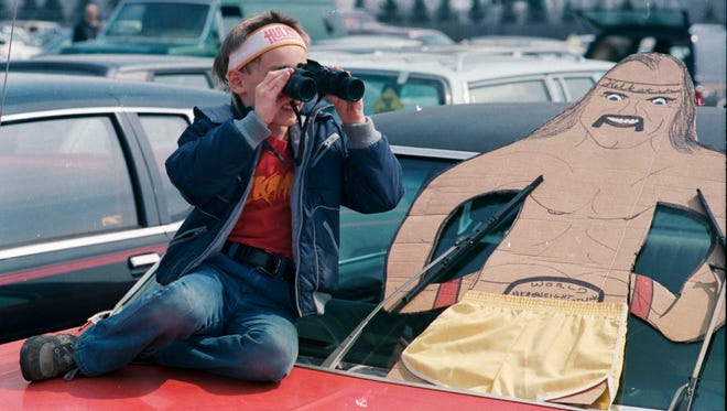 A young wrestling fan waits in the parking lot before WrestleMania III, along with his cutout of  Hulk Hogan.