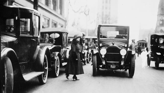 A woman walks toward the front of a car with a Michigan license plate, possibly in Detroit, circa 1915-1925. People accustomed to strolling the streets in the horse age often had problems judging the speed of automobiles.