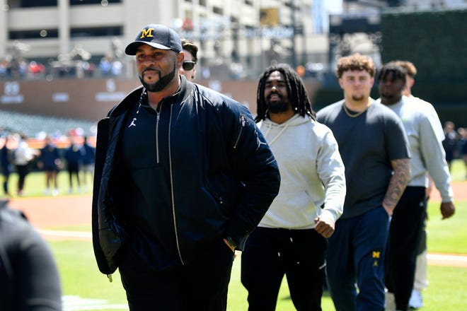 Michigan football head coach Sherrone Moore, left, leads his players off the field before the baseball game.
