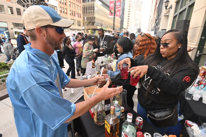 Kyle Fleischmann gets a couple drinks from Jennifer Deliane of House of Pure Vin Wine Shop along Woodward Avenue as fans enjoy the 2024 NFL Draft on the streets of Detroit.