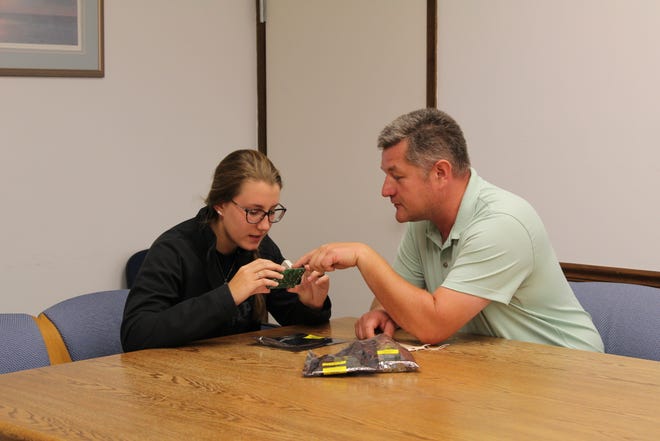 Craig Oliver, a Williams International team leader of infrastructure and facilities, explains the intricacies of a circuit board that helps expand student skills in diagnosing, troubleshooting and maintaining manufacturing machinery in his role as a mentor to Emily Eggart, a Michigan Advanced Technician Training (MAT2) student and Williams apprentice.