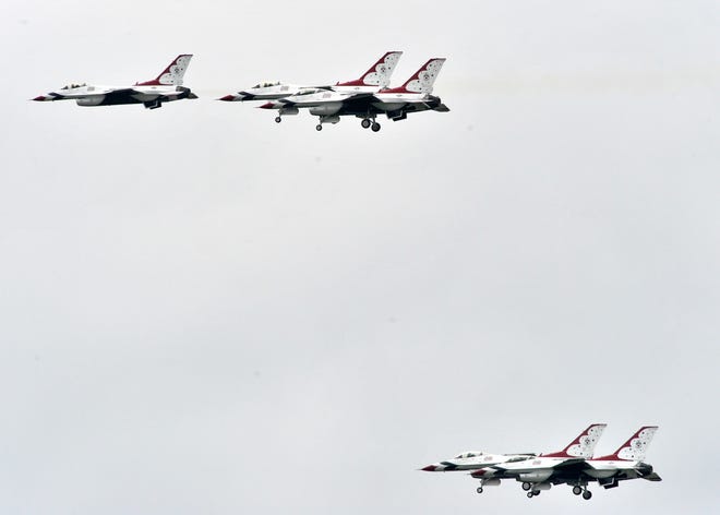 The U.S. Air Force Thunderbirds perform maneuvers in their F-16 Fighting Falcon fighter jets over the airfield as four jets spread apart as the fifth jet, left, speeds by.