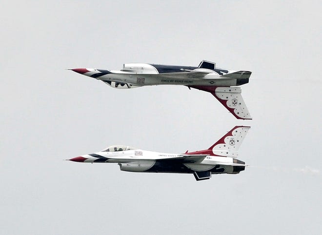 The U.S. Air Force Thunderbirds perform maneuvers in their F-16 Fighting Falcon fighter jets over the airfield as one F-16 flies inverted over the other jet.