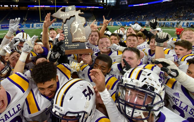Members of the Warren De La Salle football team hold up the Division 2 Championship trophy for the second consecutive year at Ford Field Friday, November 23, 2018.  They defeated Muskegon Mona Shores, 29-16.
