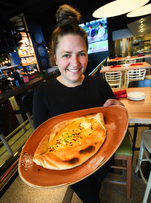 Chef and owner Emmele Herrold holding a hot plate of Georgian Cheese Bread with egg, chive and red pepper flakes.