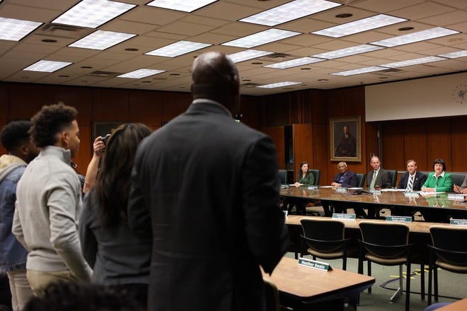 Newly-hired Michigan State University head football coach Mel Tucker and his wife and sons face the MSU Board of Trustees and university president Samuel Stanley (center)  during a special meeting Wednesday.