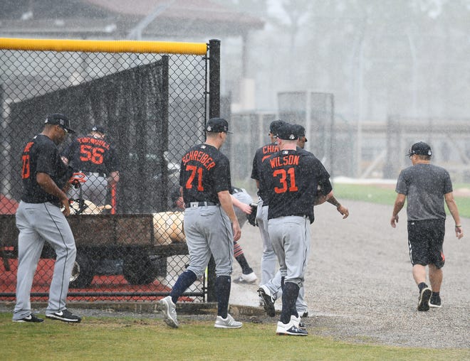 From left, Tigers pitchers Sandy Baez, John Schreiber, Alex Wilson and others seek refuge from a hard rain that temporarily stops the workout.