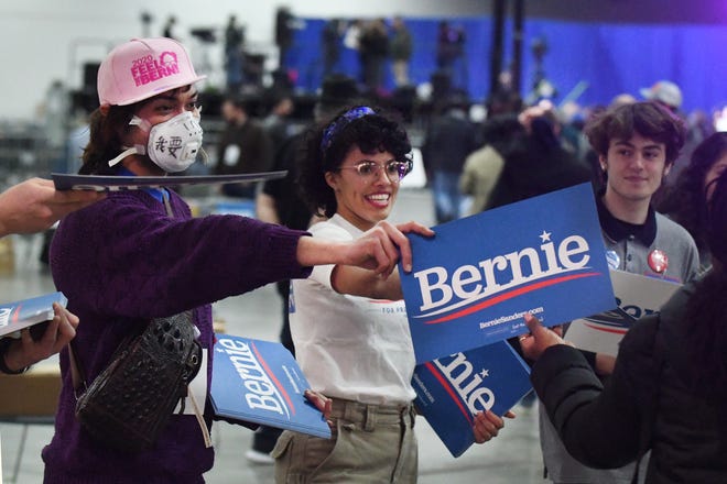 Volunteers Jayce Bixka of Westland, who is making a statement about freedom of speech by wearing a mask, and Julia Henry of Royal Oak hand out signs before Presidential candidate Bernie Sanders speaks at TCF Center in Detroit.