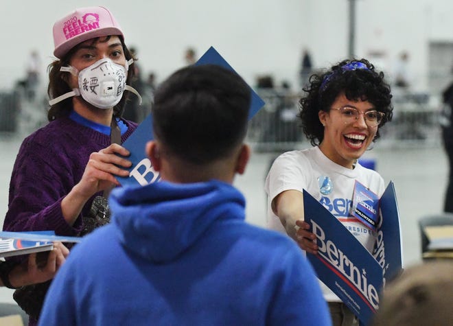 Volunteers Jayce Bixka of Westland, who is making a statement about freedom of speech by wearing a mask, and Julia Henry of Royal Oak hand out signs before Presidential candidate Bernie Sanders speaks at TCF Center in Detroit.