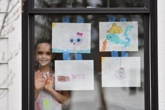 Evie Szirtes, 8, is photographed with some of her artwork taped up in the front windows of her family's home in Pleasant Ridge, Mich. on April 27, 2020.  Szirtes, home from school now like all Michigan students, usually attends Cranbrook Lower Schools Brookside has been doing these drawings as part of her schoolwork at home.
