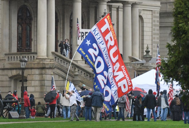 A protester makes his way around the front of the Capitol with a huge " Trump for President " sign during the " American Patroit Rally, " in Lansing.