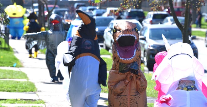 Characters walk in line as members of the Ferndale T-Rex Walking Club put on their inflatable costumes and get exercise while walking around the south end of Ferndale, Friday afternoon, May 1, 2020. All the while social distancing, they hope to bring cheer to neighbors along the route.