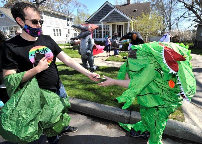 Mike Crimando, left, hands a cell phone back to his wife, Keely, both of Ferndale, as they put on their T-Rex costumes. Members of the Ferndale T-Rex Walking Club put on their inflatable costumes and get exercise while walking around the south end of Ferndale, Friday afternoon, May 1, 2020. All the while social distancing, they hope to bring cheer to neighbors along the route.
