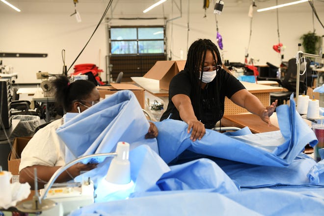 From left, Seamstresses Amber Hinton, 26, holds the material while Angel Tyler, 34, both of Detroit spreads out medical gown pieces at Empowerment Plan in Detroit on May 14, 2020.