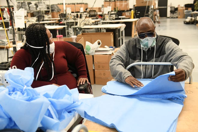 Seamstress Marie Dobine, 23, left, and inventory and logistics specialist Aaron Branch, 50, both of Detroit examine material for medical gowns that is slightly different than their last batch being produced at Empowerment Plan in Detroit on May 14, 2020.
