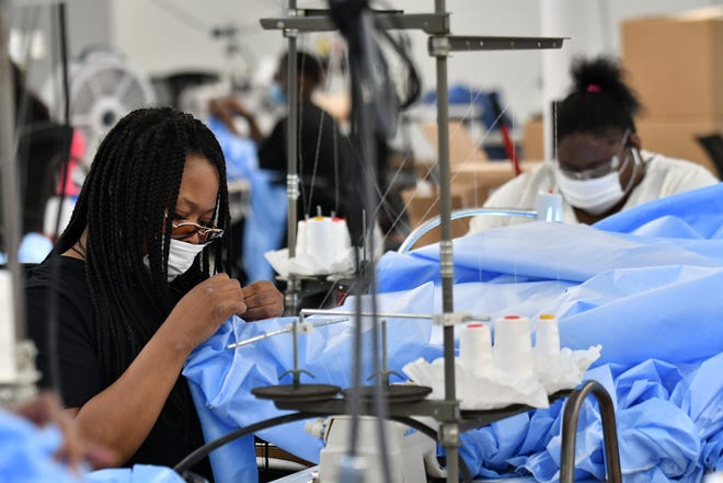 From left, Stitcher Angel Tyler, 34, inspects the seam on one of the medical isolation gowns while Amber Hinton, 26, sews at Empowerment Plan in Detroit on May 14, 2020.