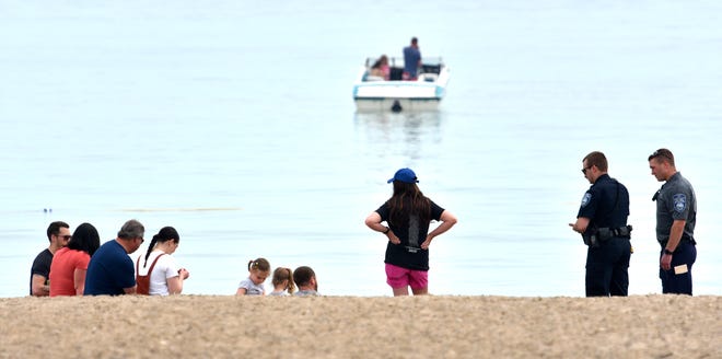 A Port Huron police officer and cadet, right, talk to beachgoers to make sure they are from the same family, which they are.