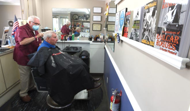 Owner Karl Manke, left, cuts the hair of Mike Calhoun, of Owosso, Tuesday afternoon, with books, written by the barber, on display on the wall.