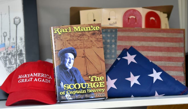 A Make America Great Again hat, a folded U.S. flag and 48-star U.S. flag are gifts to barber Karl Manke that he displays on a shelf next to a book he authored called, 'The Scourge of Captain Seavey The Great Lakes Greatest Pirate.'