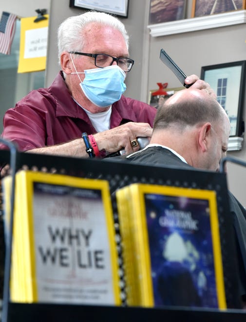 Owner Karl Manke, left, cuts the hair of Jaimie Storey, of Midland. In the foreground is a copy of the June 2017 issue of National Geographic with the headline, ' Why We Lie. The science behind our complicated relationship with the truth, ' by Yudhijit Bhattacharjee.