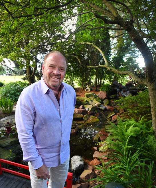 Steven, who owns a digital manufacturing company in Wixom, stands on a red bridge over a stream that leads to a koi pond.