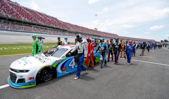 Nascar drivers Kyle Busch, left, and Corey LaJoie, right, join other drivers and crews as they push the car of Bubba Wallace to the front of the field.