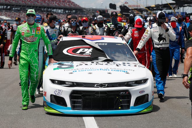 Nascar drivers Kyle Busch, left, and Corey LaJoie, right, join other drivers and crews as they push the car of Bubba Wallace to the front of the field prior to the start of Monday's race.