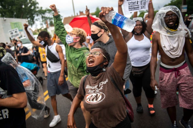 Protesters raise their fists while marching along West McNichols Road during the protest in response to a Detroit Police Department officers' fatal shooting of a 20-year-old man who shot at the police earlier in the day.