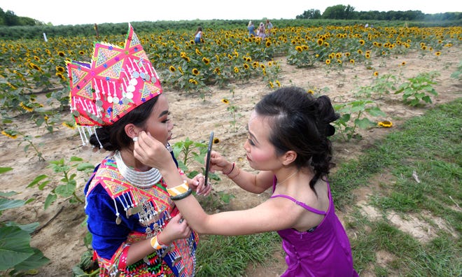 Maichoua Lor, left, gets help from her sister, Maisee Lor, both of Detroit, as they put on traditional Hmong New Year's Eve celebration clothing before taking pictures among the sunflowers.