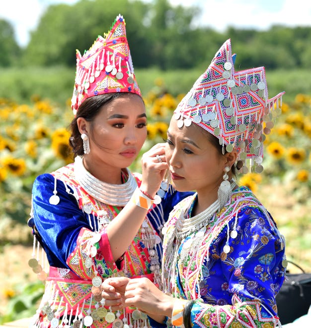 Maichoua Lor, left, helps from her sister, Maisee Lor, both of Detroit, as they put on traditional Hmong New Year's Eve celebration clothing before taking pictures among the sunflowers.