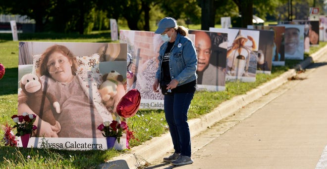 Volunteer Margaret Gore of St. Clair Shores straightens balloons attached to the portrait of COVID-19 victim Alyssa Calcaterra of Madison Heights along The Strand.