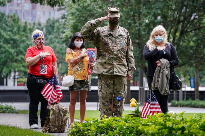 U.S. Army Sgt. Edwin Morales, center right, salutes after placing flowers for fallen FDNY firefighter Ruben D. Correa at the National September 11 Memorial and Museum, Friday, Sept. 11, 2020, in New York.  The names of nearly 3,000 victims of the Sept. 11, 2001 terror attacks will be read by family members at a ceremony organized by the Tunnel to Towers Foundation.