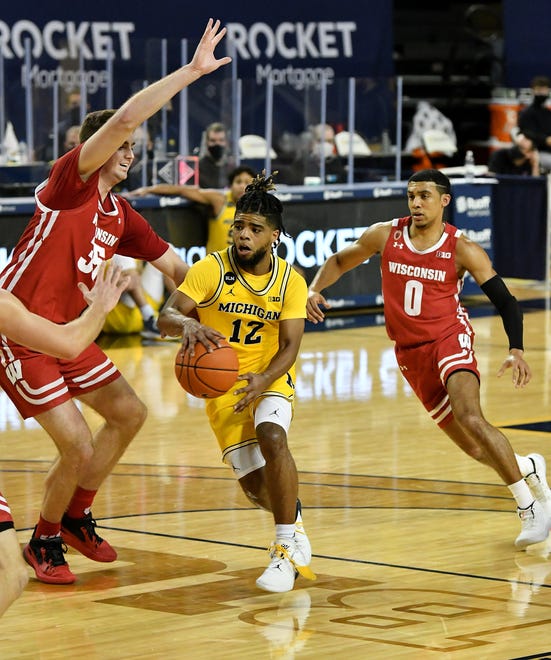Michigan guard Mike Smith (12) passes the ball around Wisconsin forward Nate Reuvers (35) being chased by Wisconsin guard D'Mitrik Trice (0) in the second half.  Michigan vs Wisconsin at Crisler Center in Ann Arbor, Mich. on Jan. 12, 2021.  Michigan wins, 77-54.