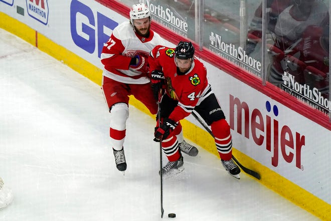 Chicago Blackhawks defender Calvin de Haan, right, controls the puck next to Detroit Red Wings center Michael Rasmussen during the third period of an NHL hockey game in Chicago, Friday, Jan. 22, 2021. The Blackhawks won 4-1. (AP Photo/Nam Y. Huh)
