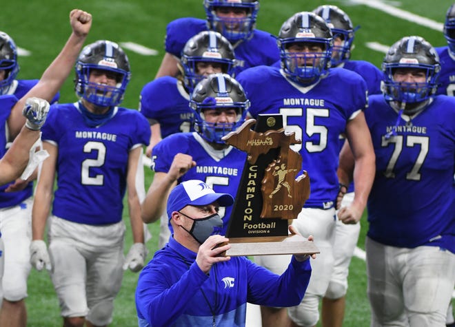 Montague head coach Patrick Collins holds up the Division 6 championship trophy after beating Clinton 40-14.