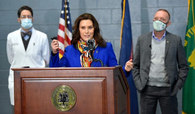 Gov. Gretchen Whitmer, center, holds up her mask as she answers questions from reporters as Oakland County Chief Medical Officer Dr. Russell Faust, left, and Oakland County Executive Dave Coulter listen in Pontiac, Friday, April 2, 2021.