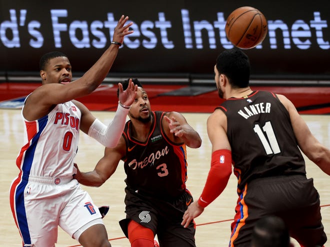 Detroit Pistons guard Dennis Smith Jr., left, passes the ball past Portland Trail Blazers guard CJ McCollum, center, and center Enes Kanter during the first half of an NBA basketball game in Portland, Ore., Saturday, April 10, 2021.