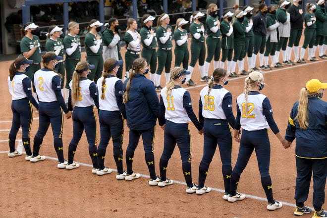 Michigan and Michigan State players line the first and third base lines for the playing of the National Anthem before their game.