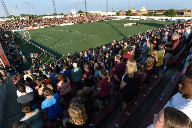 Detroit City FC and L.A. Force players, along with a full Keyworth Stadium, stand for the national anthem.