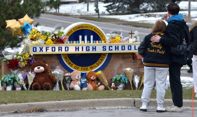 Students console each other as they put flowers at a makeshift memorial at an Oxford High School sign outside the school on Wednesday, Dec. 1, 2021, a day after four students were killed and seven others, including a teacher, were wounded in a mass shooting.