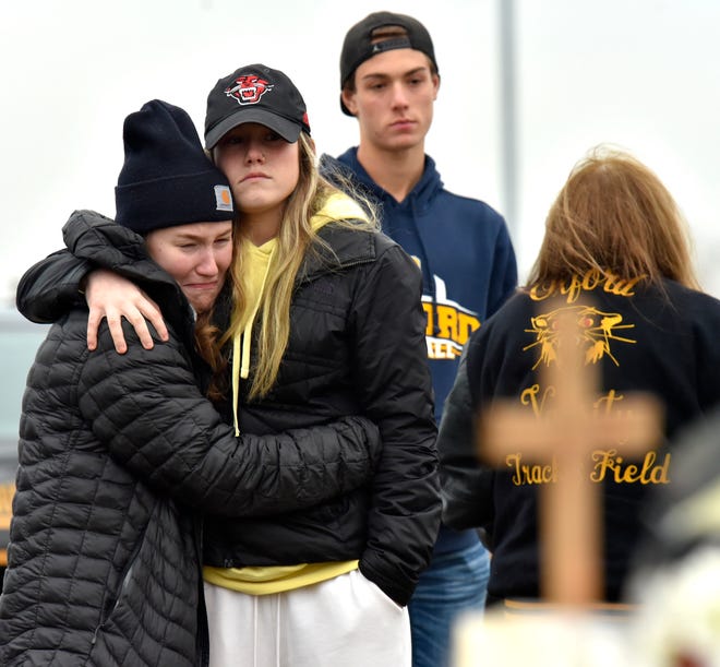 Students cry and console each other as they put flowers at a makeshift memorial at an Oxford High School sign outside the school on Wednesday, Dec. 1, 2021, a day after four students were killed and seven others, including a teacher, were wounded in a mass shooting.