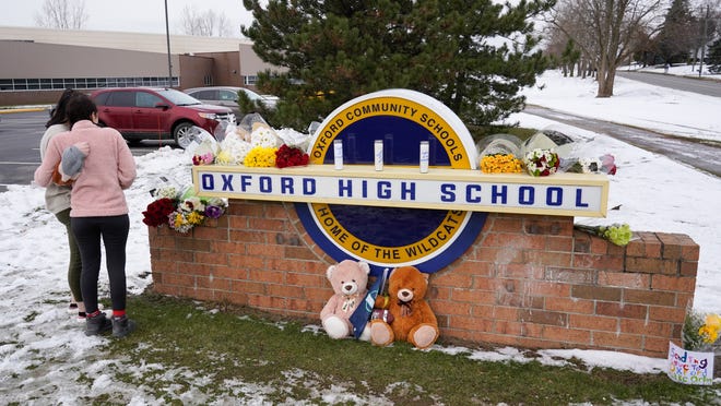 Students stand at the sign of Oxford High School where memorial items are being placed on Wednesday, Dec. 1, 2021, a day after four students were killed and seven others, including a teacher, were wounded in a mass shooting.