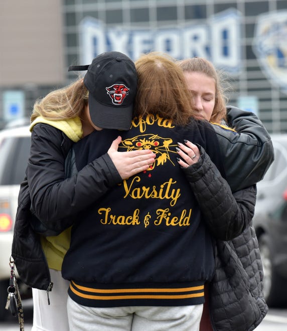 Students cry and console each other as they put flowers at a makeshift memorial at an Oxford High School sign outside the school, on Wednesday, Dec. 1, 2021, a day after four students were killed and seven others, including a teacher, were wounded in a mass shooting.
